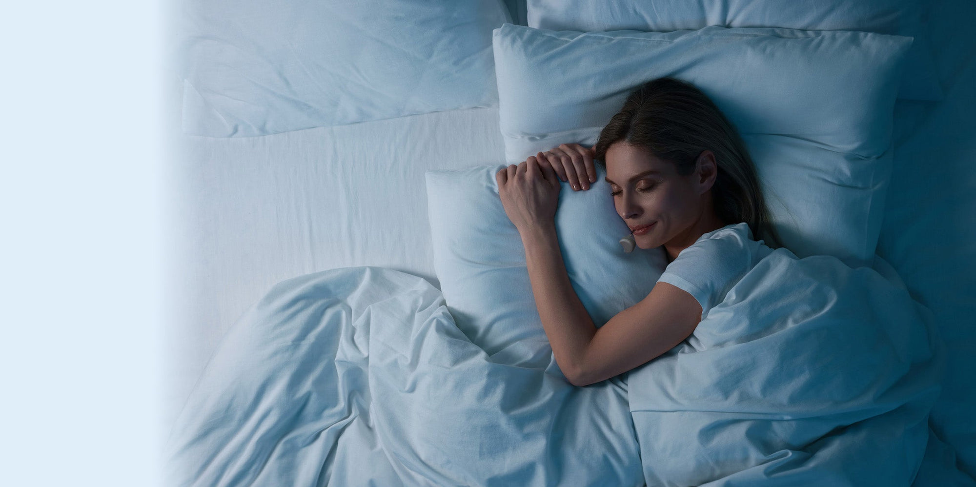 Woman sleeping peacefully in a bed with white bedding wearing a Zerene mouthguard.