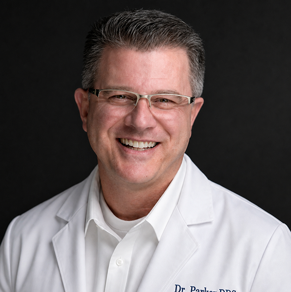 Man wearing glasses and a white coat with 'Dr. Parker DDS' on a black background