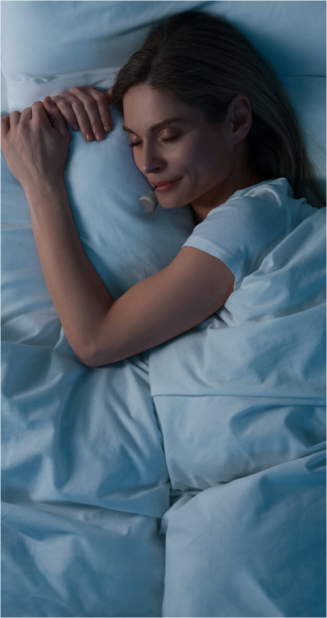 Woman sleeping peacefully in a bed with white bedding wearing a Zerene mouthguard.