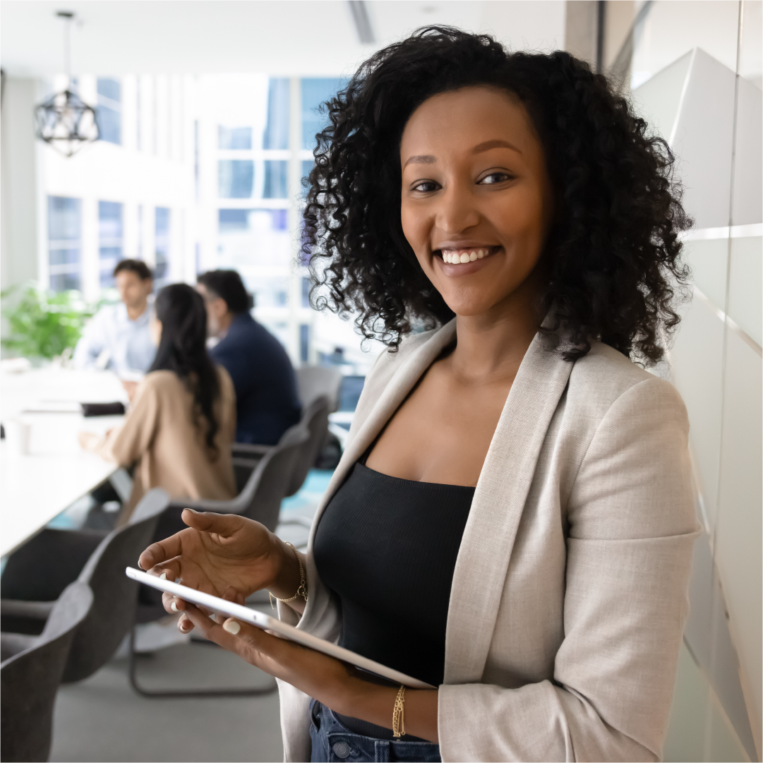 Woman holding a tablet in an office setting with colleagues in the background